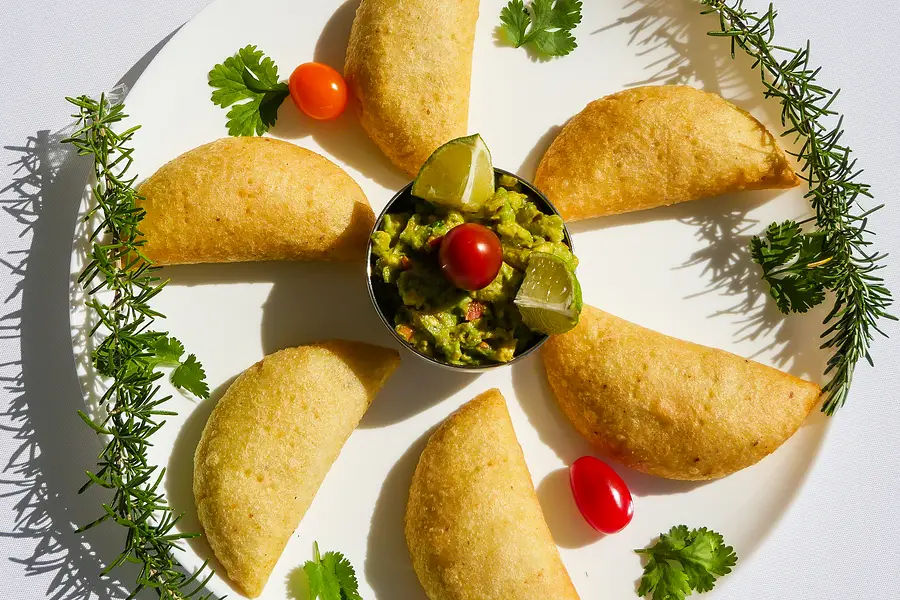Des empanadas en cercle sur une assiette blanche, autour du guacamole